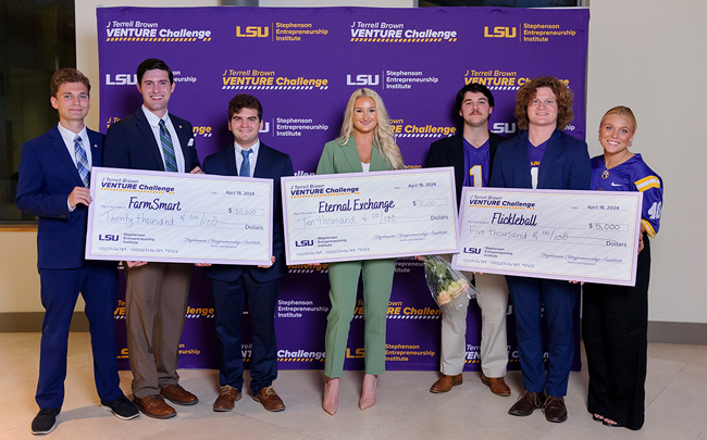 Students hold giant cardboard checks and smile with excitement as prizes are distributed on stage at the 2024 J Terrell Brown Venture Challenge.