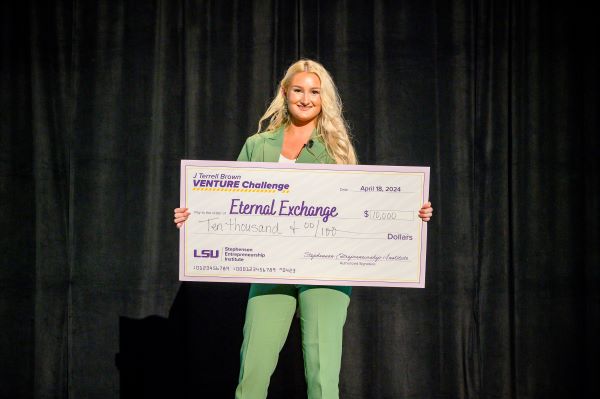 Woman in green suit hold large check for ten thousand dollars. 