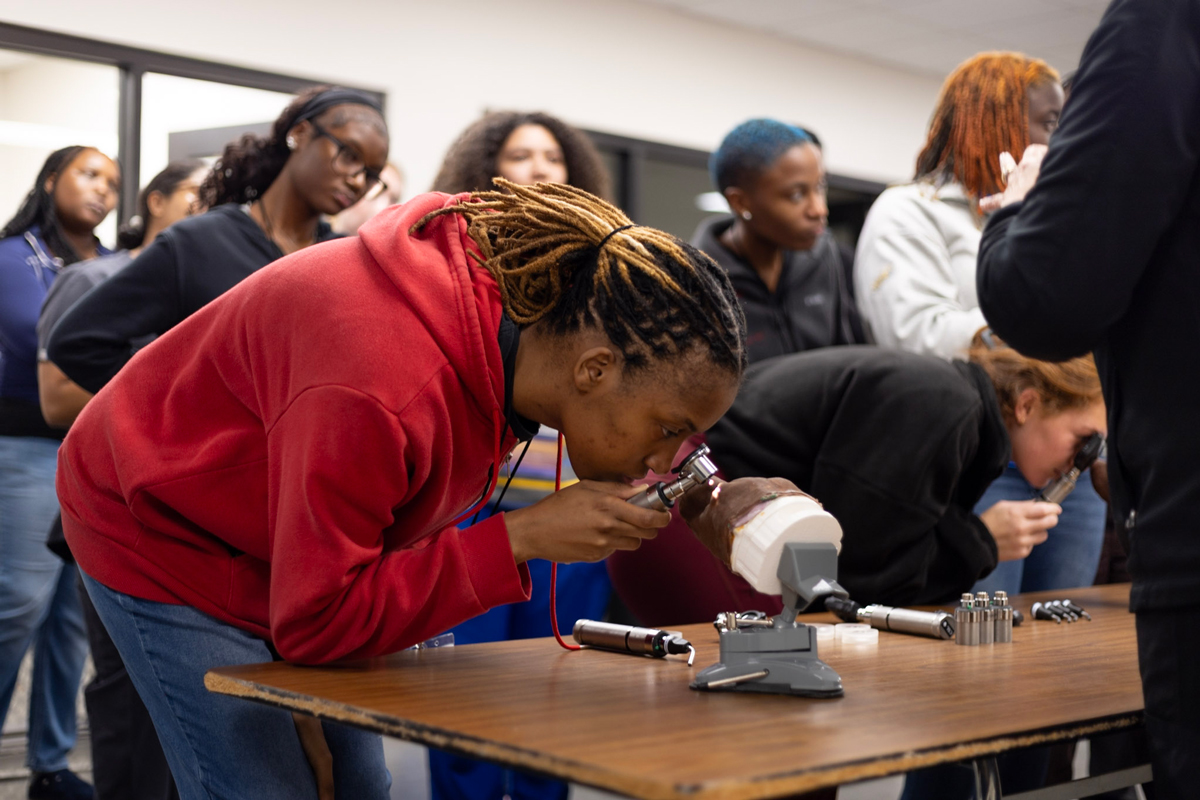student looking through an otoscope at a dog head model